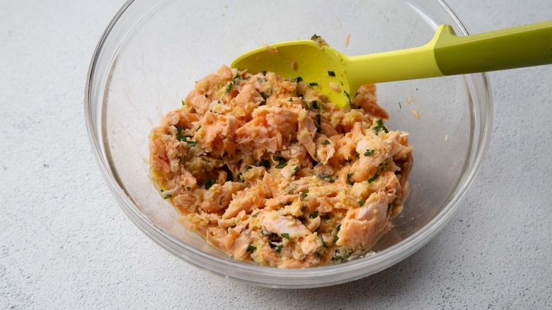 Flaked cooked salmon and parsley in a clear bowl with a rubber spatula