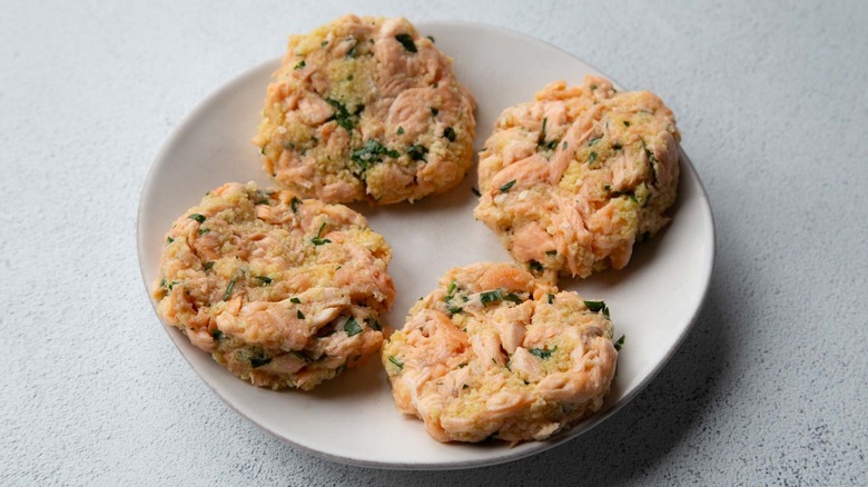 Four uncooked salmon patties on a white plate