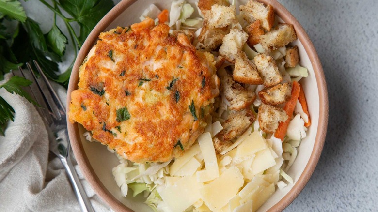 Salmon burger with coleslaw, croutons, and cheese in a beige bowl