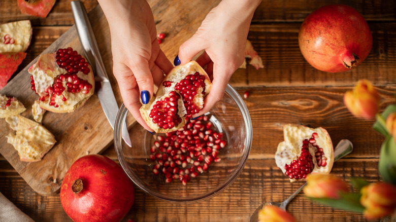 Person pulling out pomegranate seeds from fruit