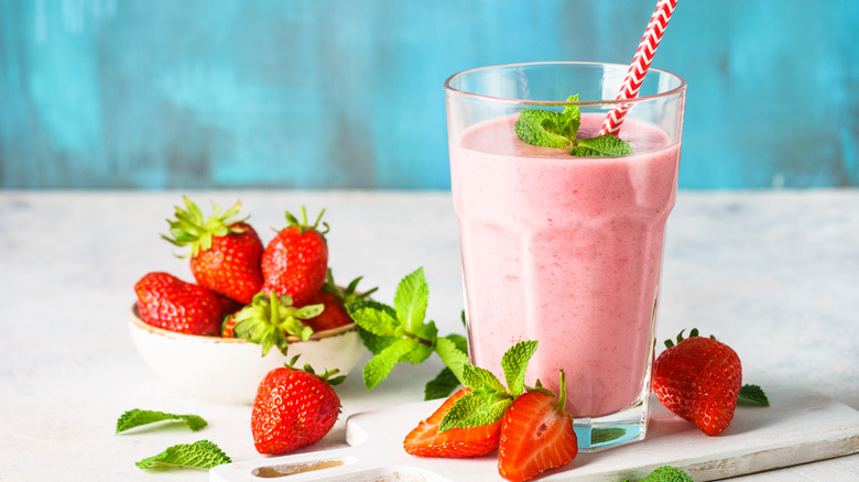 Pink drink in a glass surrounded by strawberries