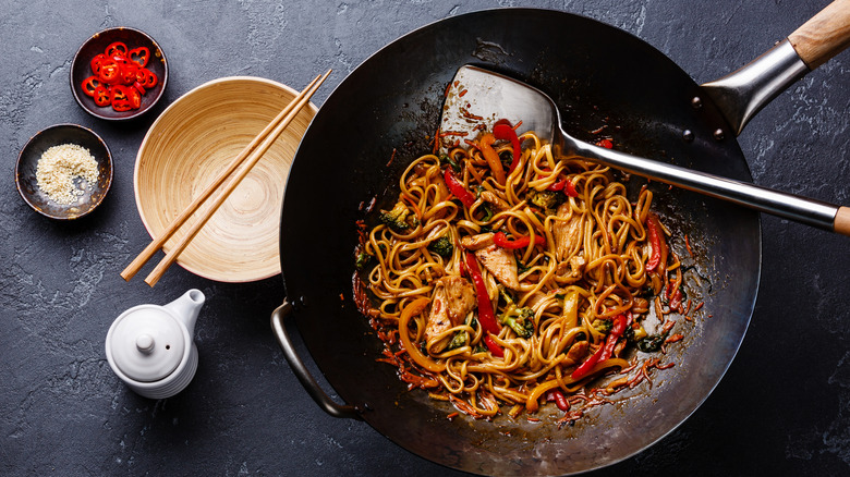 stir-fry noodles in wok next to bowl with chopsticks on granite counter