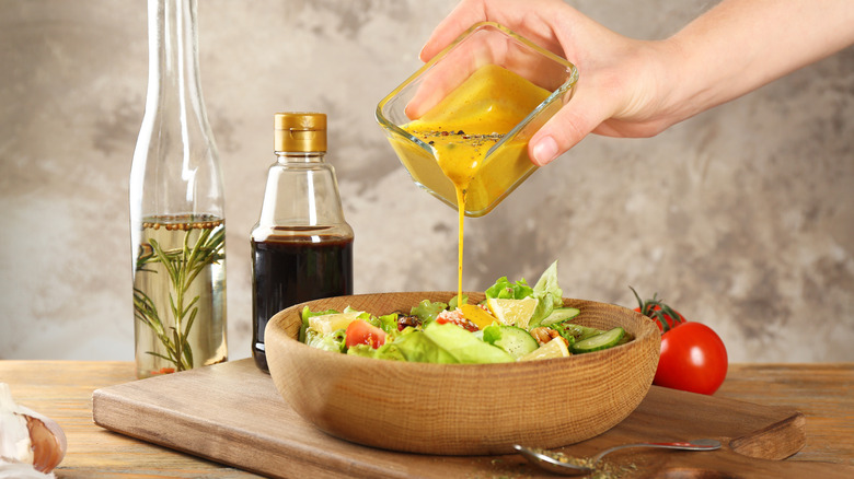 A person pours salad dressing on a salad