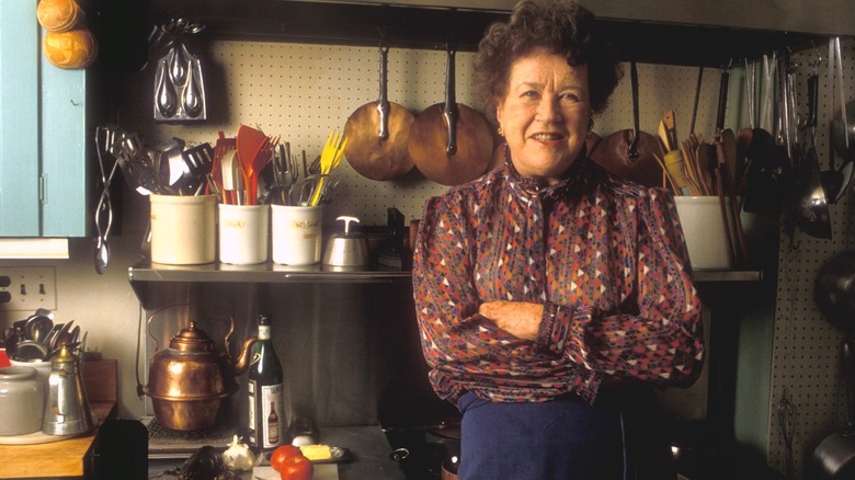 Julia Child posing against kitchen wall.