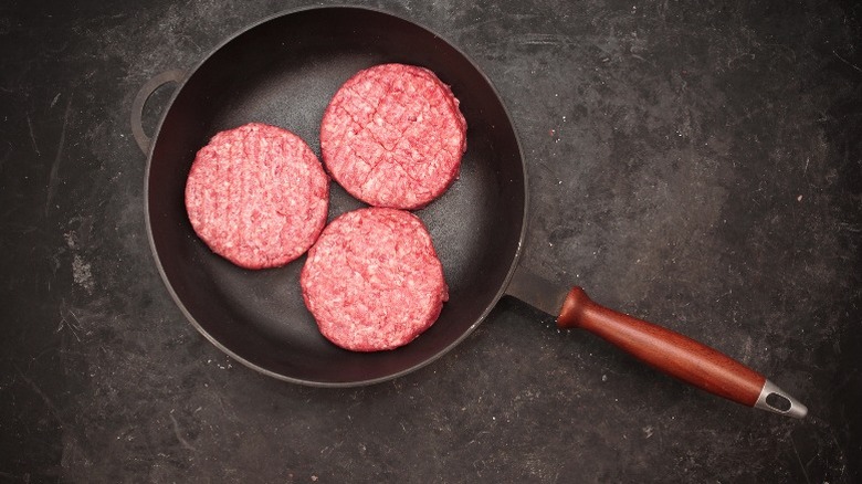 Three burger patties in a cast iron pan.