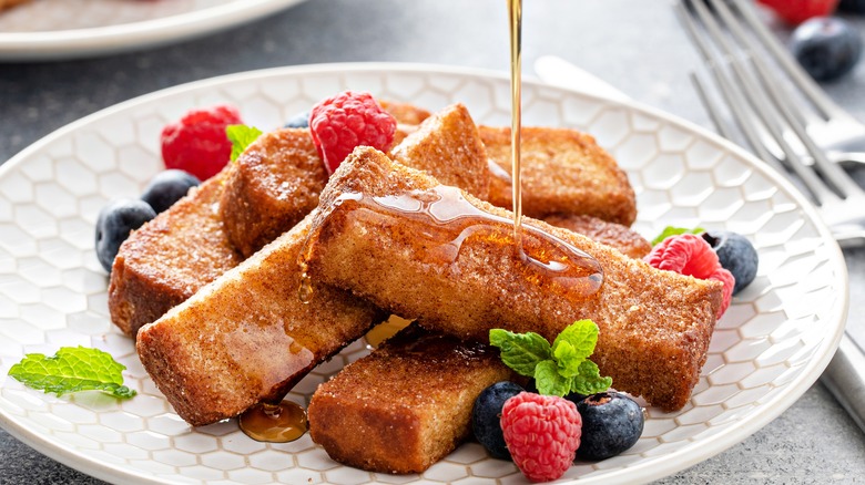 French toast sticks being covered with syrup.