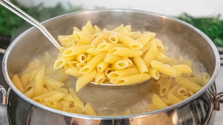 ladle of boiling penne pasta in steel pot