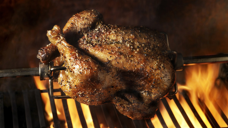 A whole turkey on a rotisserie above a grill