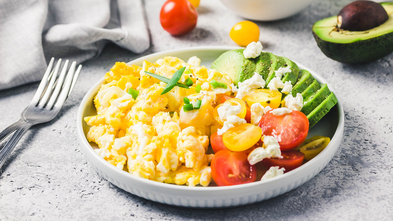 Scrambled eggs in a bowl with tomato, avocado, cheese