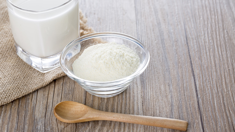 Powdered milk in bowl with wooden spoon and glass of milk