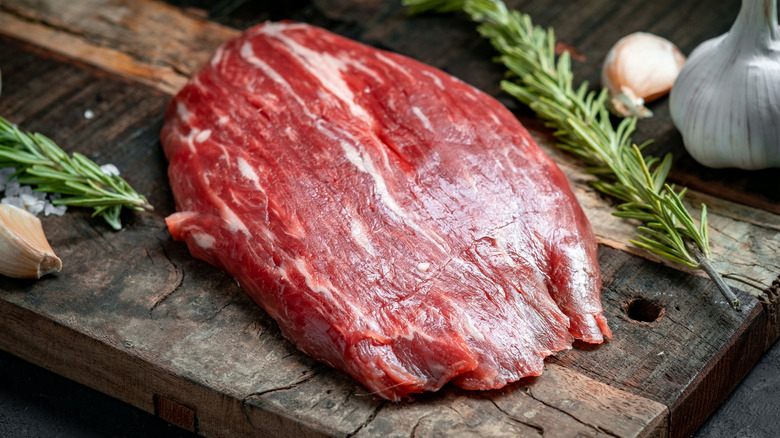 raw cut of flank steak on a wooden cutting board