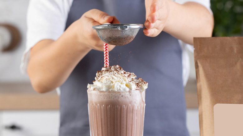 Person sprinkling cocoa over milkshake