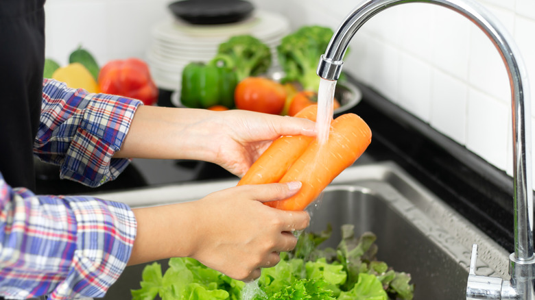 person washing carrots in sink