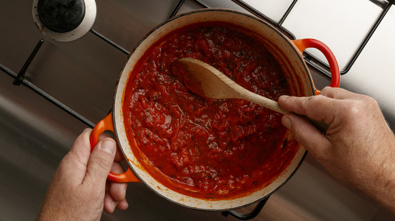 stirring pot of tomato sauce with wooden spoon