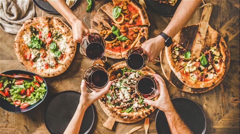 Hands with wine glasses over pizza