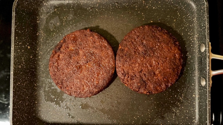 2 burgers cooking in pan