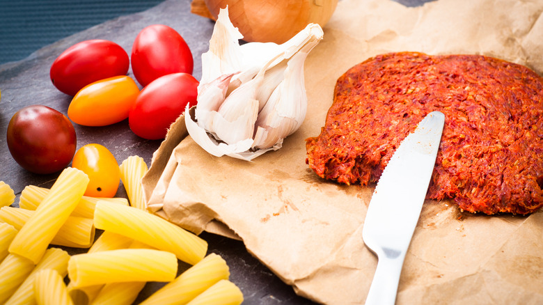 'Nduja next to garlic, tomatoes, and rigatoni pasta