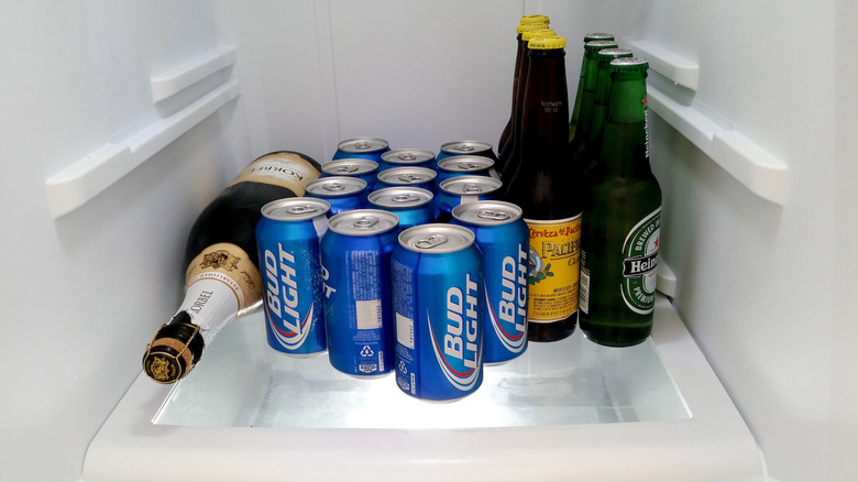 Clean white refrigerator shelf with cans of Bud Light and bottles of Pacifica and Heineken all upright and one bottle of Korbel sparkling wine on its side