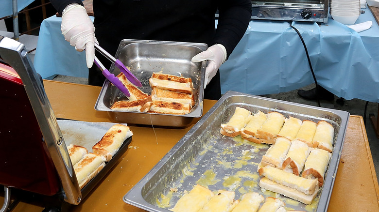 Person serving cheese rolls from metal pans