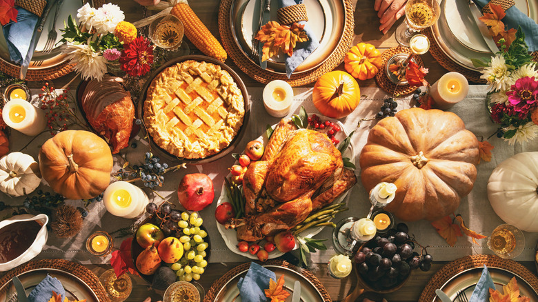 Festive holiday table with turkey, pie, gourds, plates