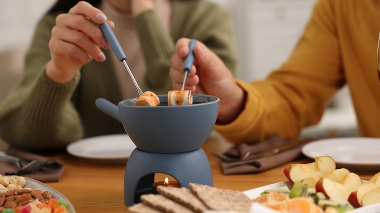 Two people dipping marshmallows into fondue