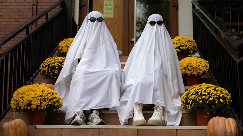 Two people in ghost costumes sit on steps
