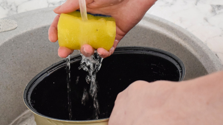 Hands washing a slow cooker with a sponge in the sink