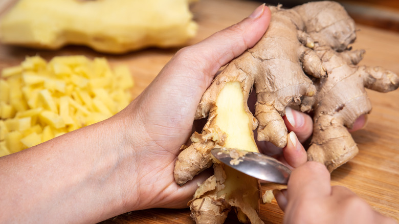 person holding and peeling ginger with a spoon