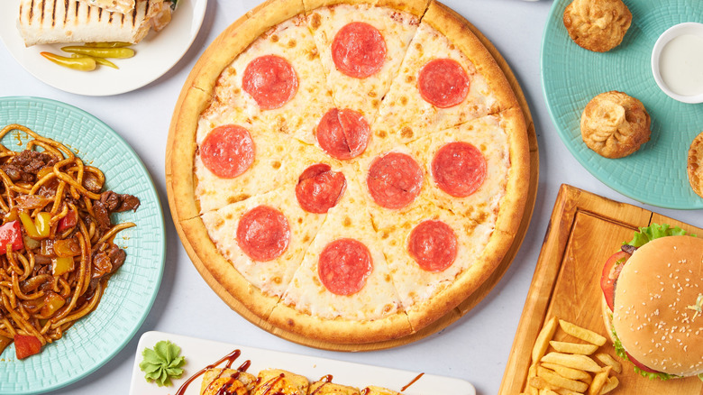 Pepperoni pizza surrounded by other foods like hamburger, noodles, and appetizer bites.