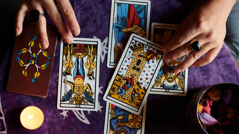 Hands surrounding five upturned tarot cards on a purple fabric