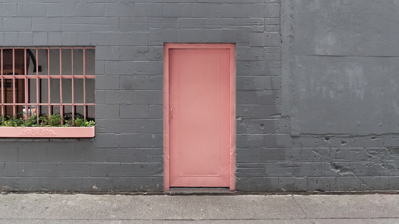 A pink door against a grey brick wall 