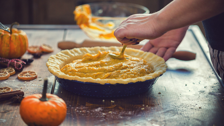 Person filling a pumpkin pie crust