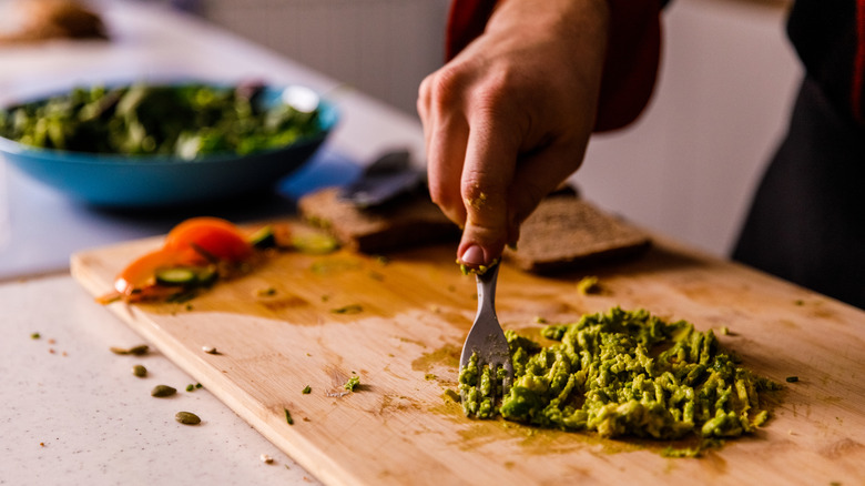 Mashing avocado with fork on cutting board