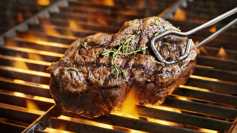 Close-up of a sirloin steak held over a grill