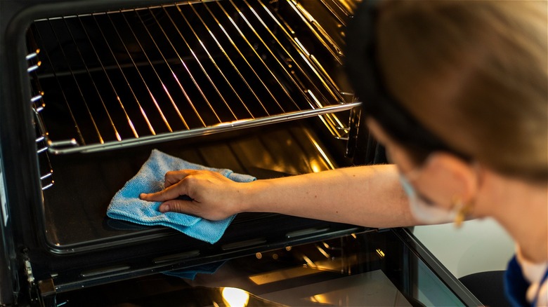 Woman wiping oven with blue towel 