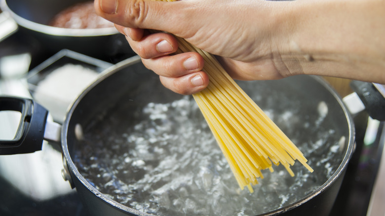 cook putting spaghetti in boiling water