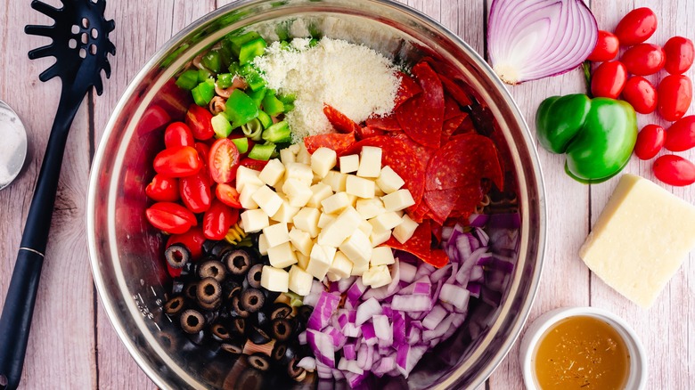 bowl of pasta salad ingredients: cheese, pepperoni, onion, olives, tomatoes