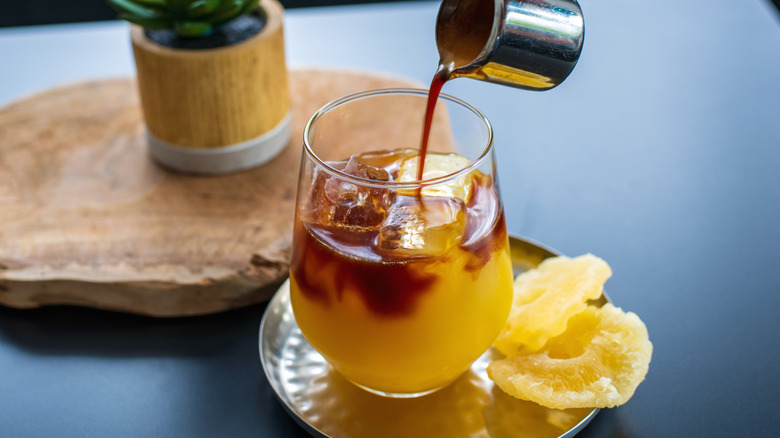 A shot of espresso being poured into a glass of pineapple juice