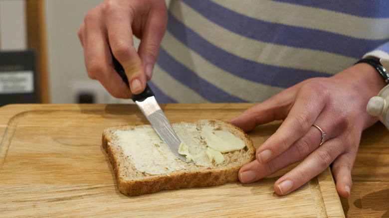 someone spreading mayo and butter on bread