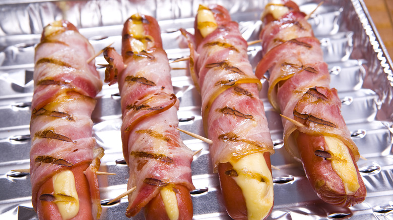 Multiple bacon-wrapped cheesy hot dogs on tin tray