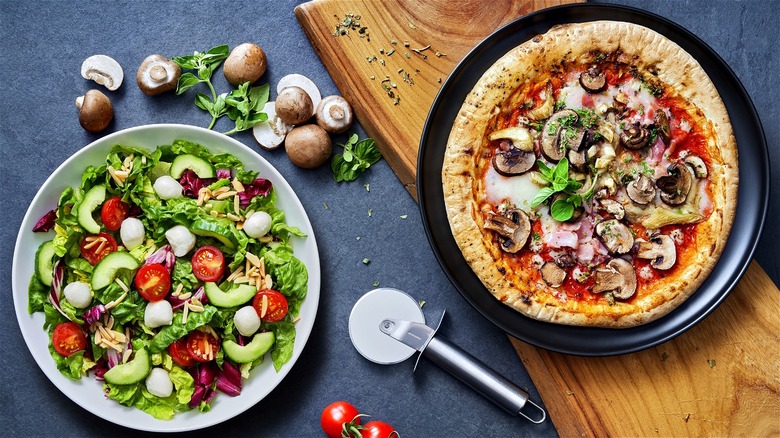 bowl of salad next to whole pizza