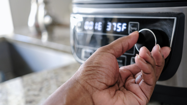 A person's hand setting air fryer temp.