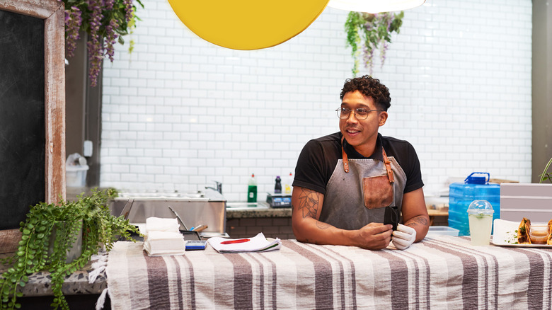 A man in an apron smiles behind a counter