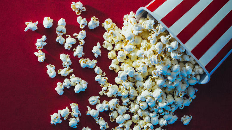 Striped bucket of popcorn spilled onto a red background