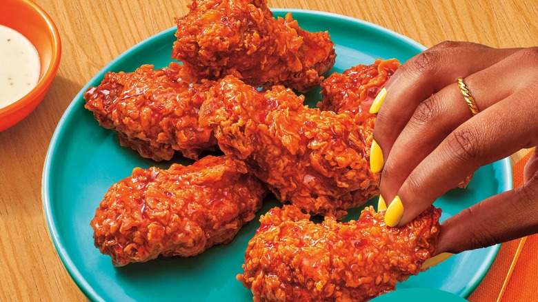 Hand grabbing a Popeyes wing from a plate