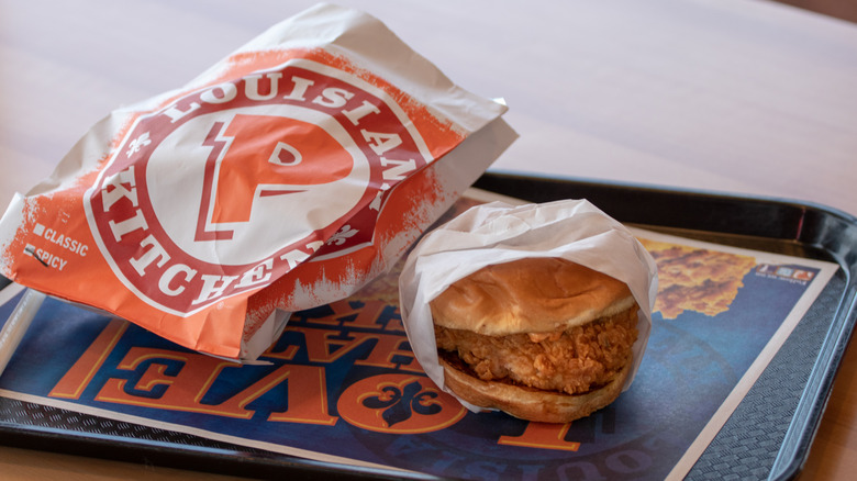 A Popeyes chicken sandwich on a tray next to its bag