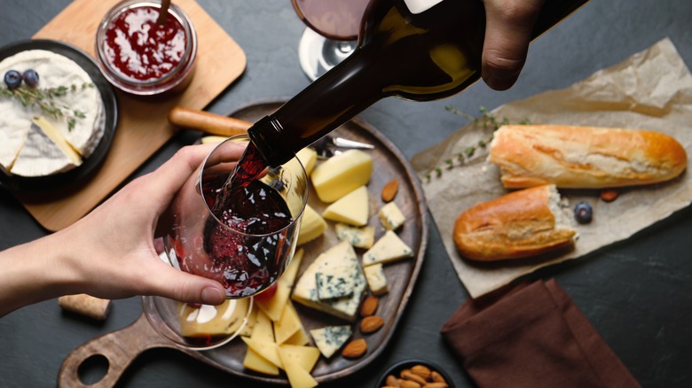 A person pours a glass of red wine over a snack board