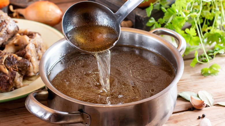 Ladle pouring beef broth into pot