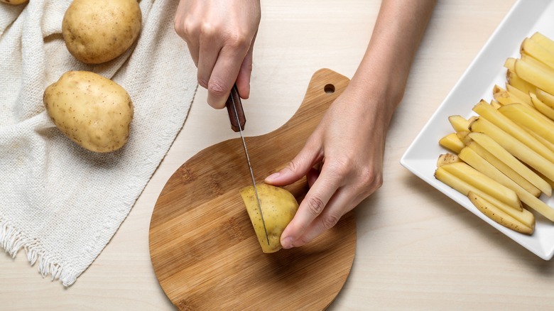 Person cutting potatoes on board