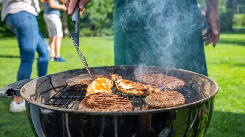 Person grilling different meats in backyard